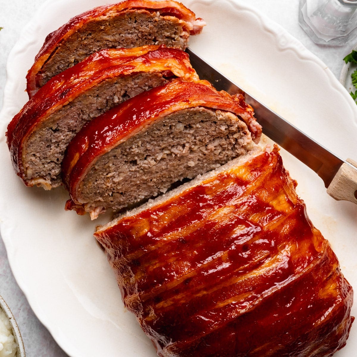 Overhead shot of a sliced bacon wrapped meatloaf on a white serving platter.